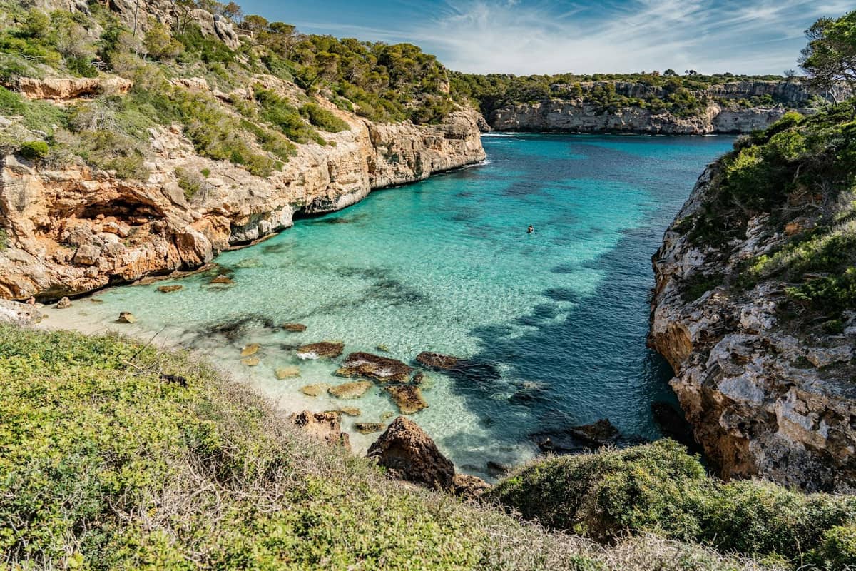 Idyllische Felsenbucht mit türkisfarbenem Wasser und üppiger Vegetation entlang der Südostküste von Mallorca, perfektes Beispiel für die wunderschönen Strände in der Region Santanyí.
