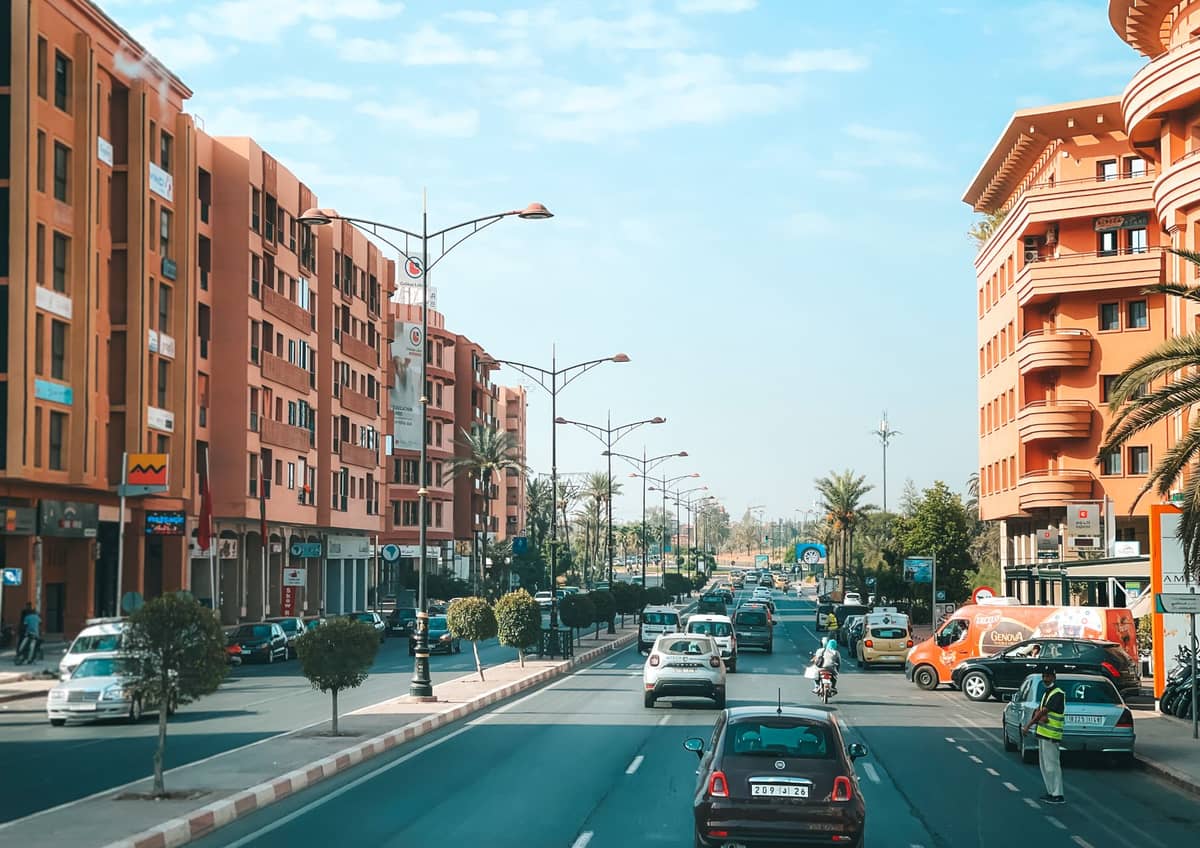 ถนนบูเลอวาร์ดกว้างในย่าน Gueliz เมือง Marrakech เรียงรายด้วยอาคารอพาร์ตเมนต์สมัยใหม่และโรงแรม มีรถยนต์วิ่งในวันที่แดดจัด พร้อมต้นปาล์มตลอดสองข้างถนน