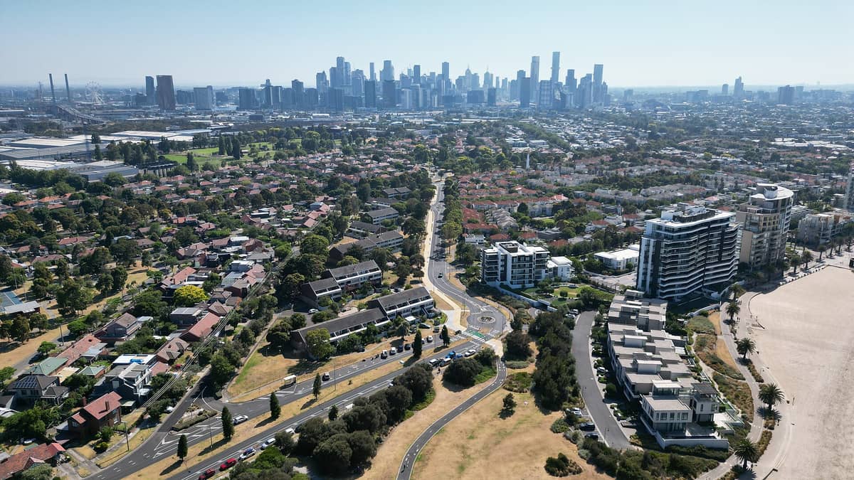 Luftaufnahme der weitläufigen Vorstadtviertel Melbournes im Vordergrund mit der Skyline der Stadt in der Ferne, die die große geografische Ausdehnung der Stadt verdeutlicht.