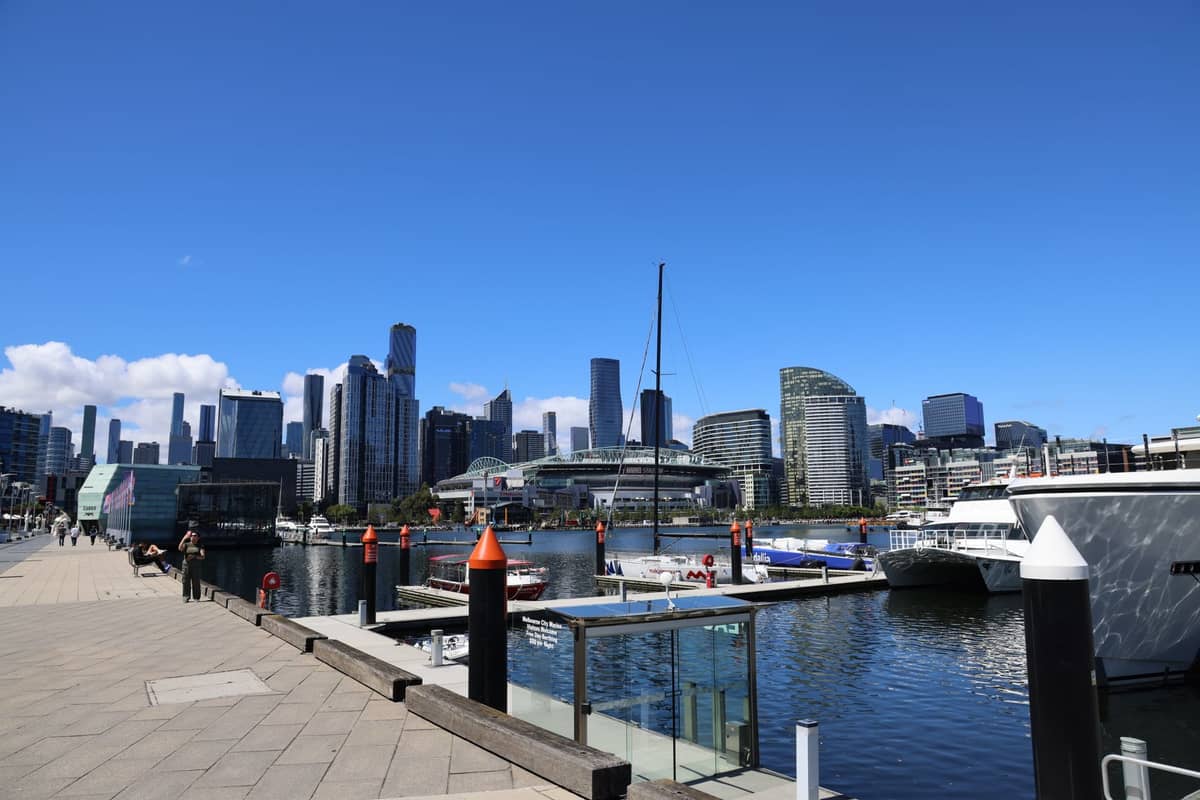 Melbourne Docklands Uferpromenade mit modernen Hochhäusern, Yachten und einem klaren blauen Himmel, von einem Fußgängerweg aus gesehen.