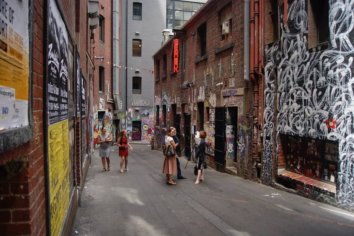 Menschen, die in einer der berühmten Gassen des Melbourne CBD spazieren und sich unterhalten, mit Street-Art an den Backsteinwänden und einer lebhaften urbanen Szene.