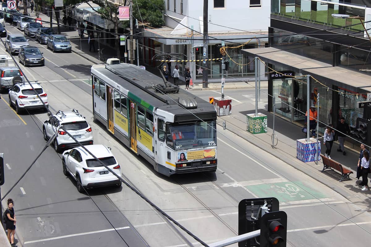 Eine Straßenbahn fährt die Chapel Street in South Yarra entlang, gesäumt von Boutiquen und geparkten Autos an einem sonnigen Tag.
