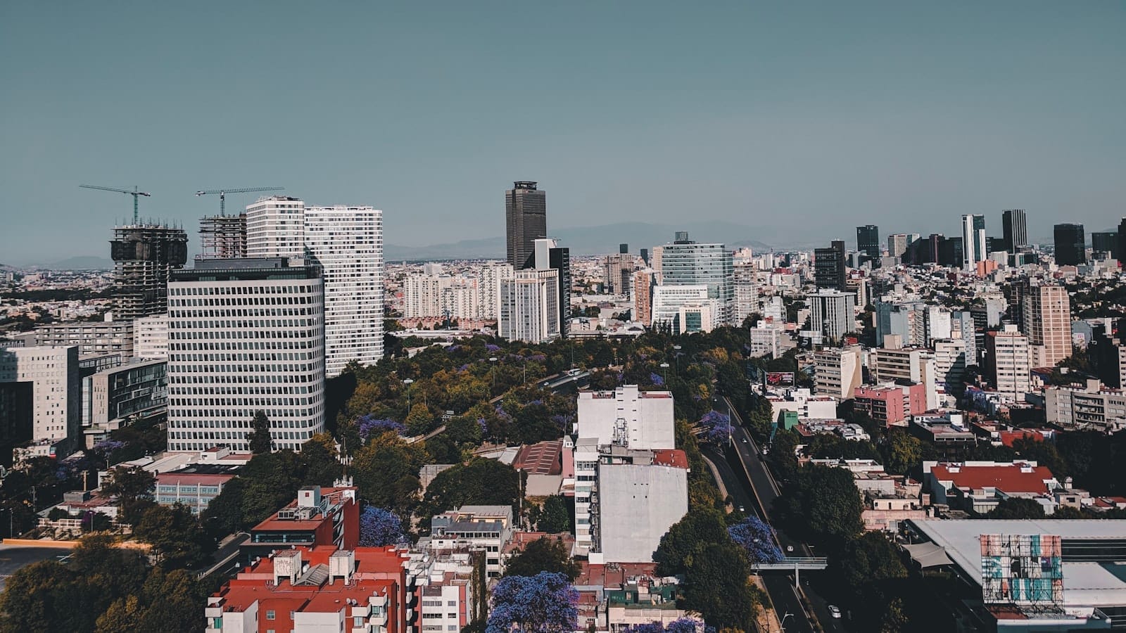 Vista aérea da Cidade do México com modernos arranha-céus, áreas residenciais e ruas arborizadas sob um céu limpo.