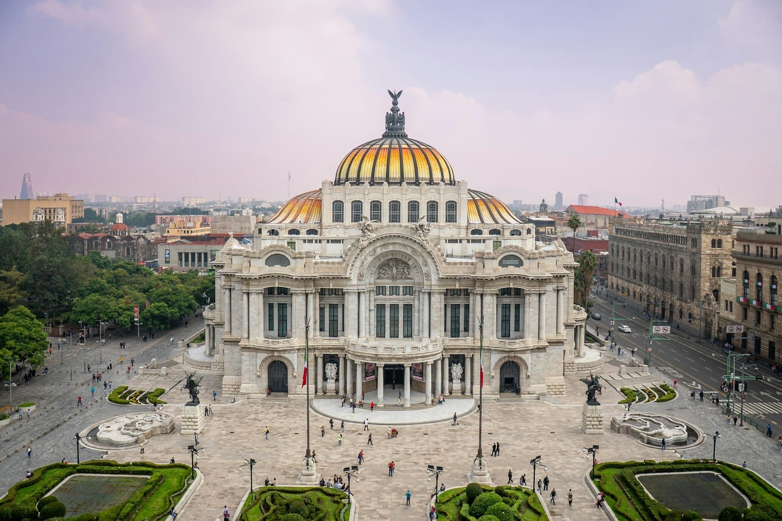 Vista aérea do Palacio de Bellas Artes no Centro Histórico da Cidade do México, com jardins e edifícios históricos sob um céu claro.