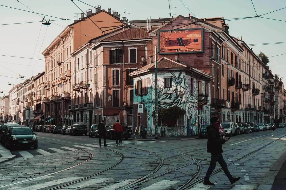 Large rue urbaine à Milan bordée d'immeubles d'appartements colorés, de rails de tramway et de street art, révélant un quartier urbain animé.