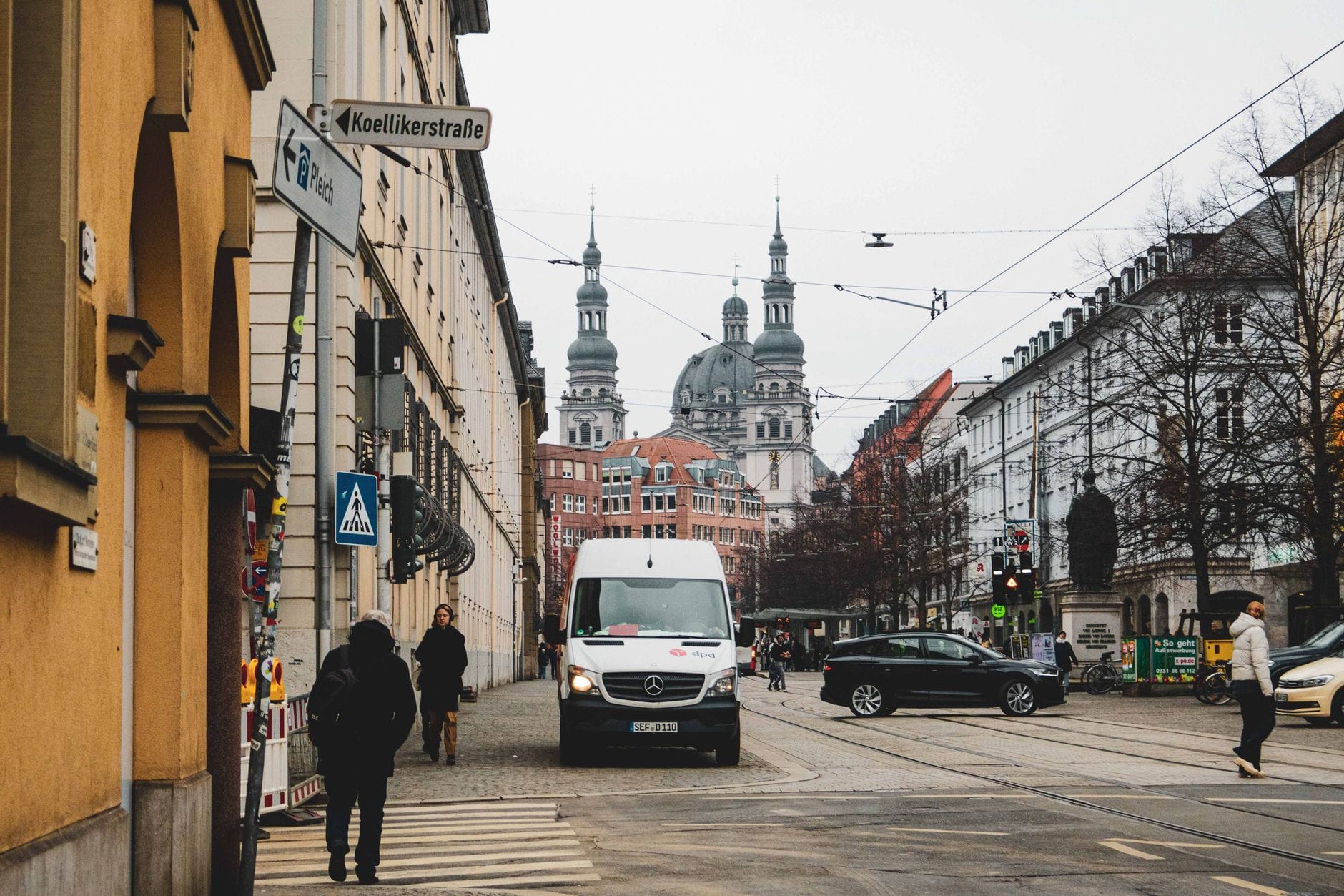 วิวถนนในเมืองที่ย่าน Haidhausen เมือง Munich พร้อมด้วยอาคารประวัติศาสตร์ ผู้คนเดินบนถนน รางรถราง และโบสถ์โดม St. Lukas อยู่เบื้องหลัง