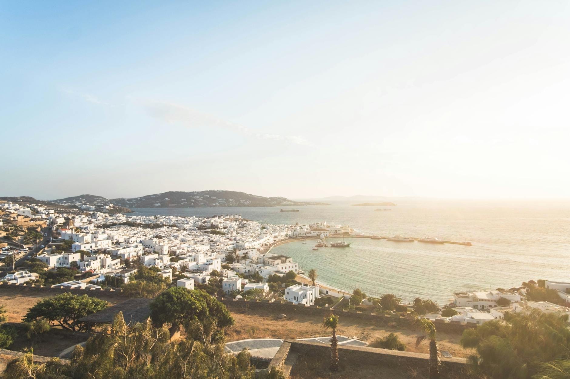 Vista panorámica de Mykonos con sus casas blancas cicládicas, el mar Egeo y un cielo dorado al atardecer, evocando el espíritu de las islas griegas.