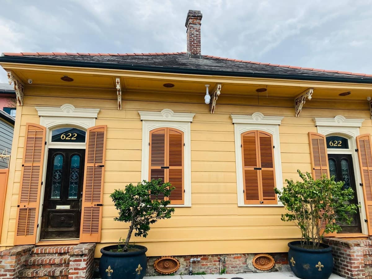Historic New Orleans shotgun house with bright yellow facade, classic shutters, and twin doors, exuding the unique charm of a local neighborhood.