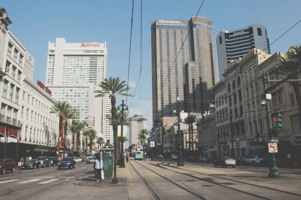 Street-level view of New Orleans Central Business District with major hotels, palm trees, streetcar tracks, and tall buildings on both sides.