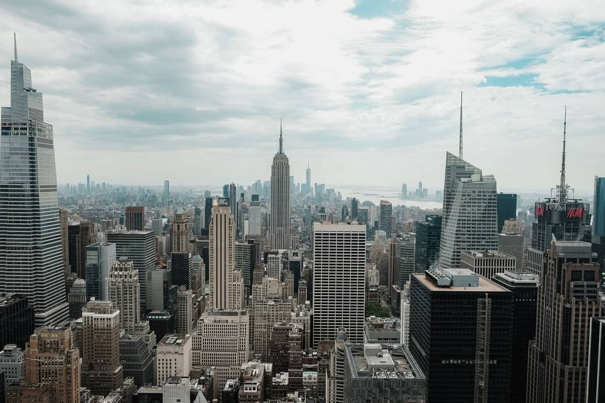Weitläufiger Blick auf die Skyline von Midtown Manhattan mit dem Empire State Building und Wolkenkratzern unter einem teils bewölkten Himmel.