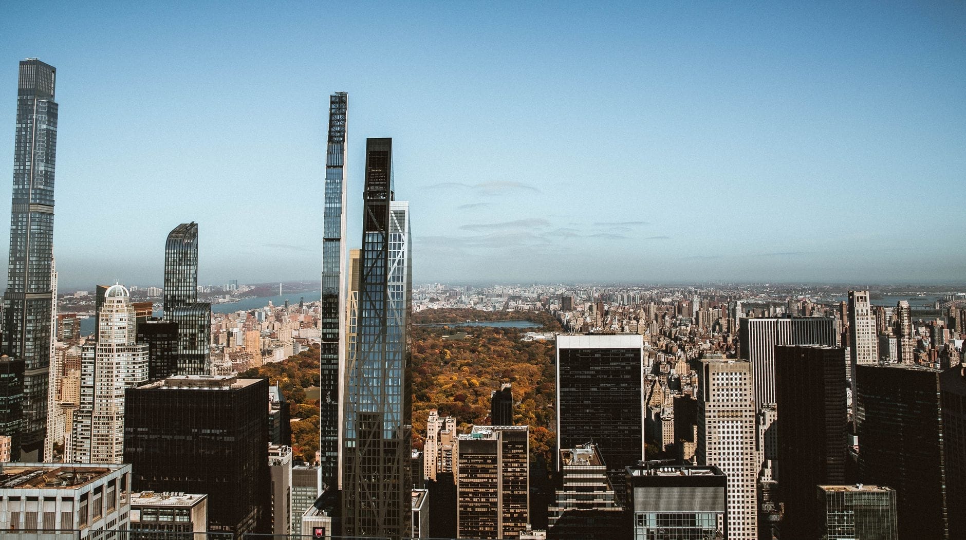 Vista panorâmica dos arranha-céus do Midtown Manhattan com o Central Park ao fundo sob um céu azul, mostrando vários bairros distintos de Nova York.