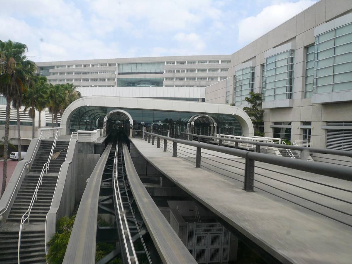 Gleise des automatischen Personentransportsystems und Terminalgebäude am Orlando International Airport mit Palmen und moderner Architektur.