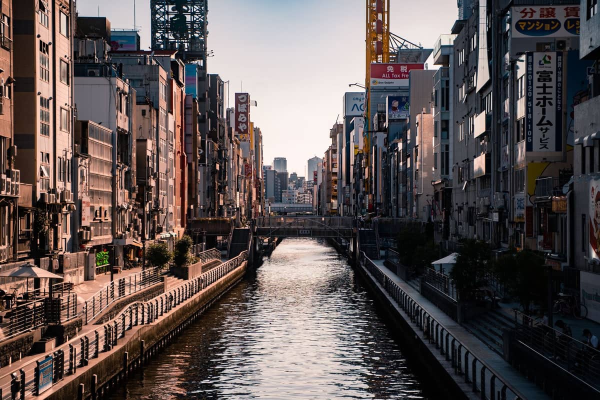 View down the Dotonbori canal framed by tall buildings and neon signs in central Osaka at dusk.