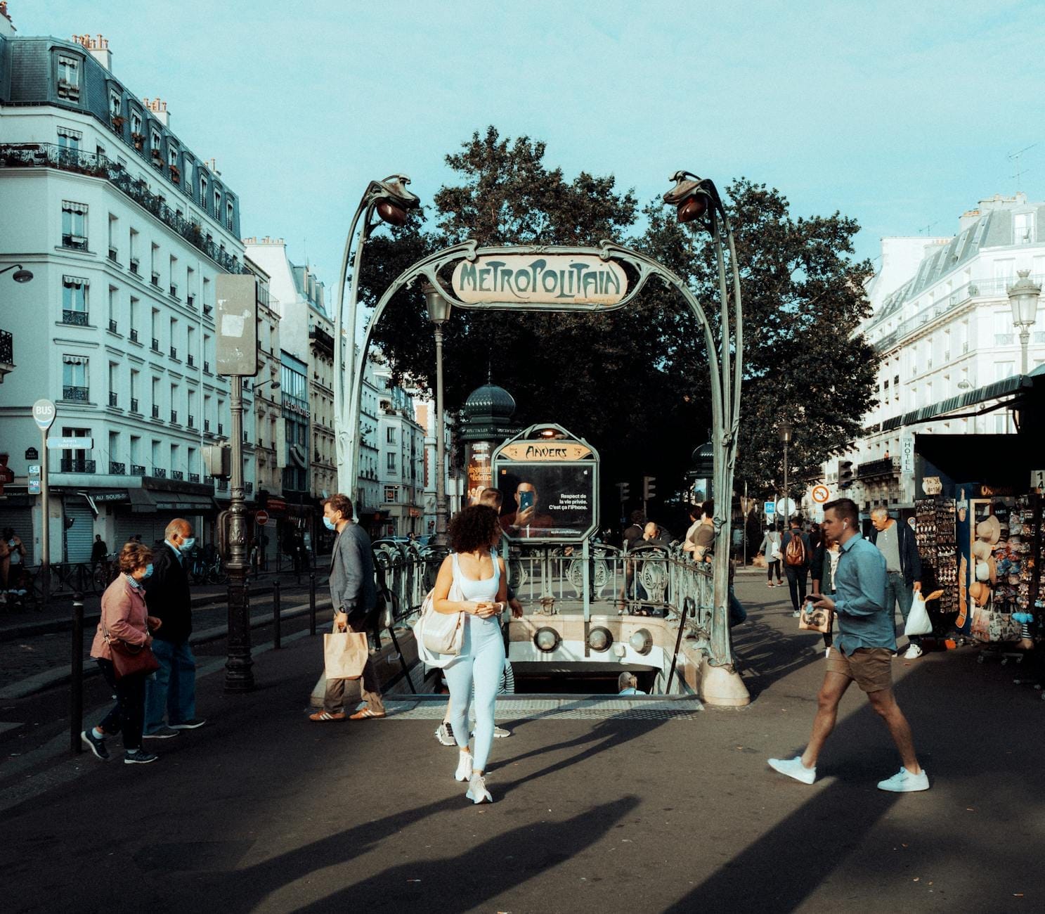 I parigini camminano davanti all'iconico ingresso art nouveau di una stazione della Métro di Parigi, circondata da tipici edifici parigini.