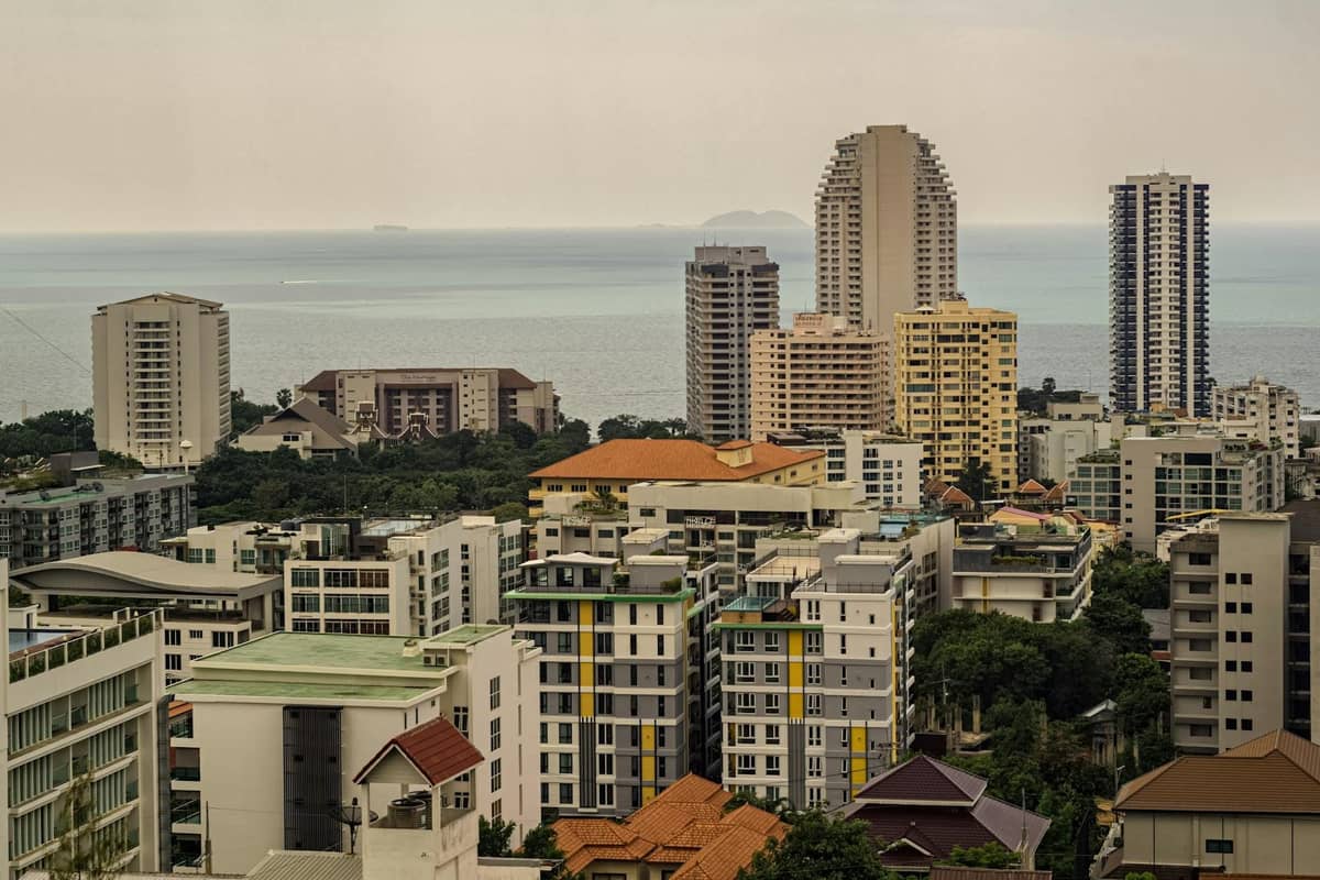 Elevated view of Pratumnak Hill in Pattaya with mid-rise condos, modern high-rise buildings, lush greenery, and the sea in the background.