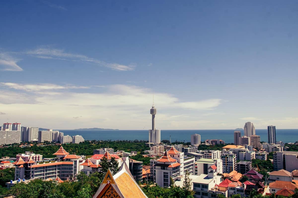 Wide view of Pattaya skyline with various modern buildings, the Pattaya tower, and coastline under a bright blue sky.