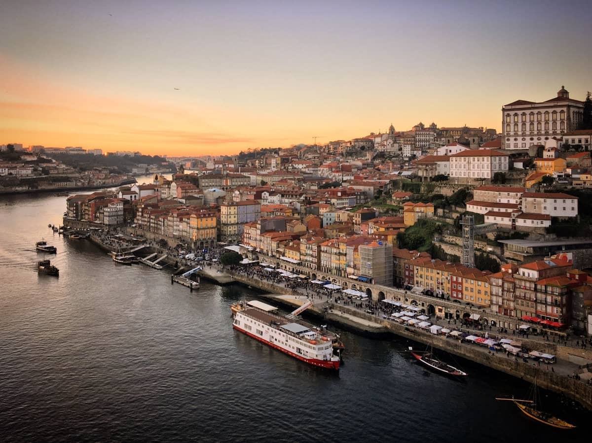 Luftaufnahme des Ribeira-Viertels in Porto mit bunten Gebäuden am Flussufer, der Promenade am Fluss Douro, Booten und Abendhimmel über der Stadt.