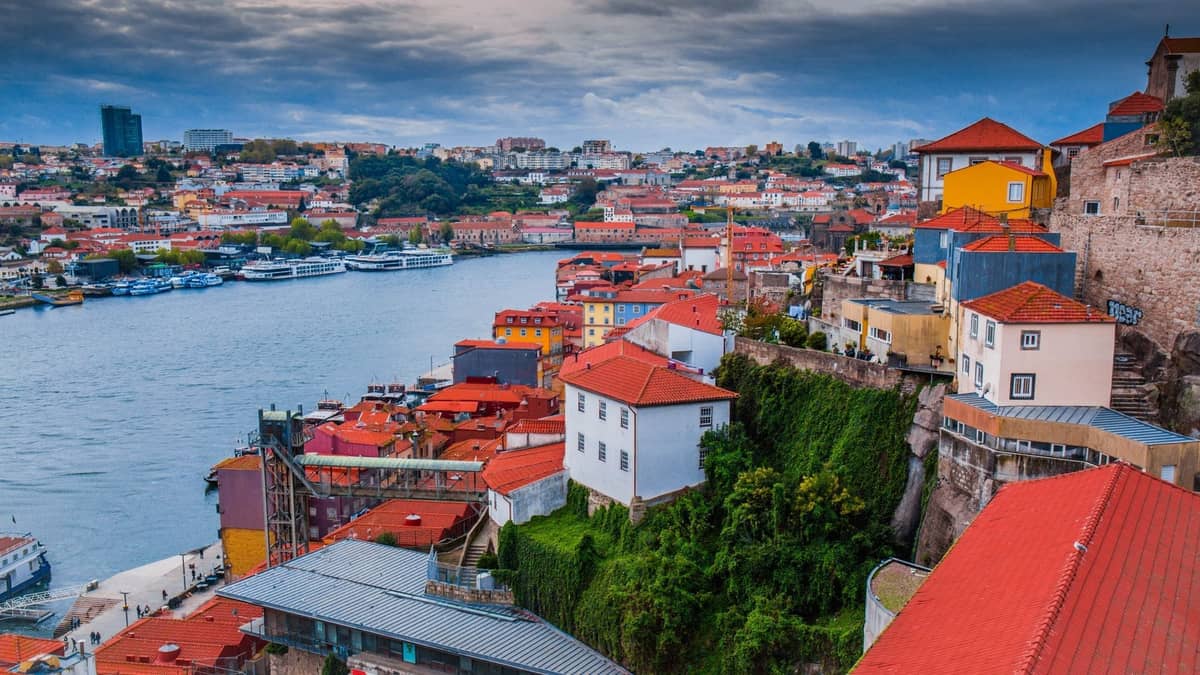 Panoramablick auf die Flussufer-Viertel von Porto mit bunten Gebäuden auf einem Hügel mit Blick auf den Douro und die Stadtsilhouette im Hintergrund.