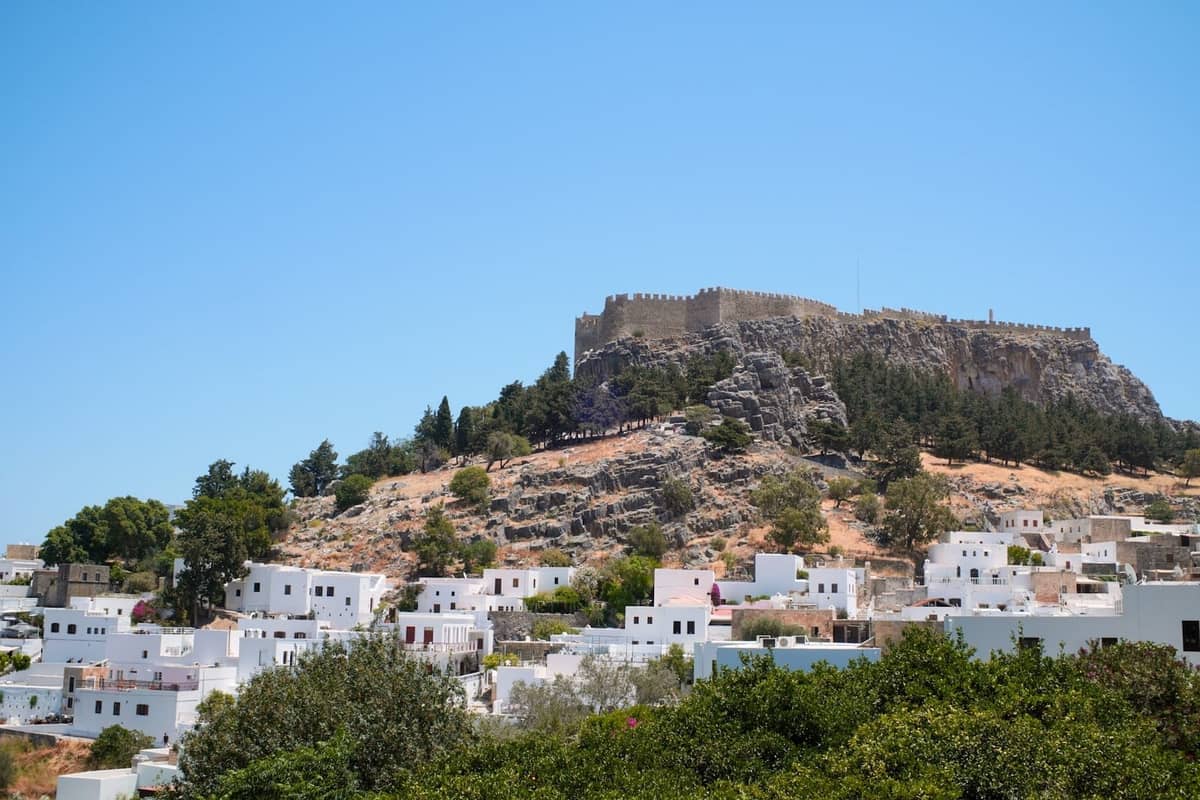 Whitewashed houses and the ancient acropolis overlooking the village of Lindos on a sunny day in Rhodes, Greece.