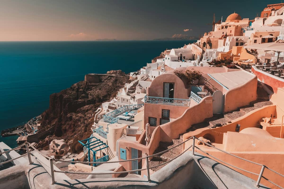 Santorini caldera village with white cycladic buildings and blue sea below, perched dramatically on the cliff edge under a clear sky.