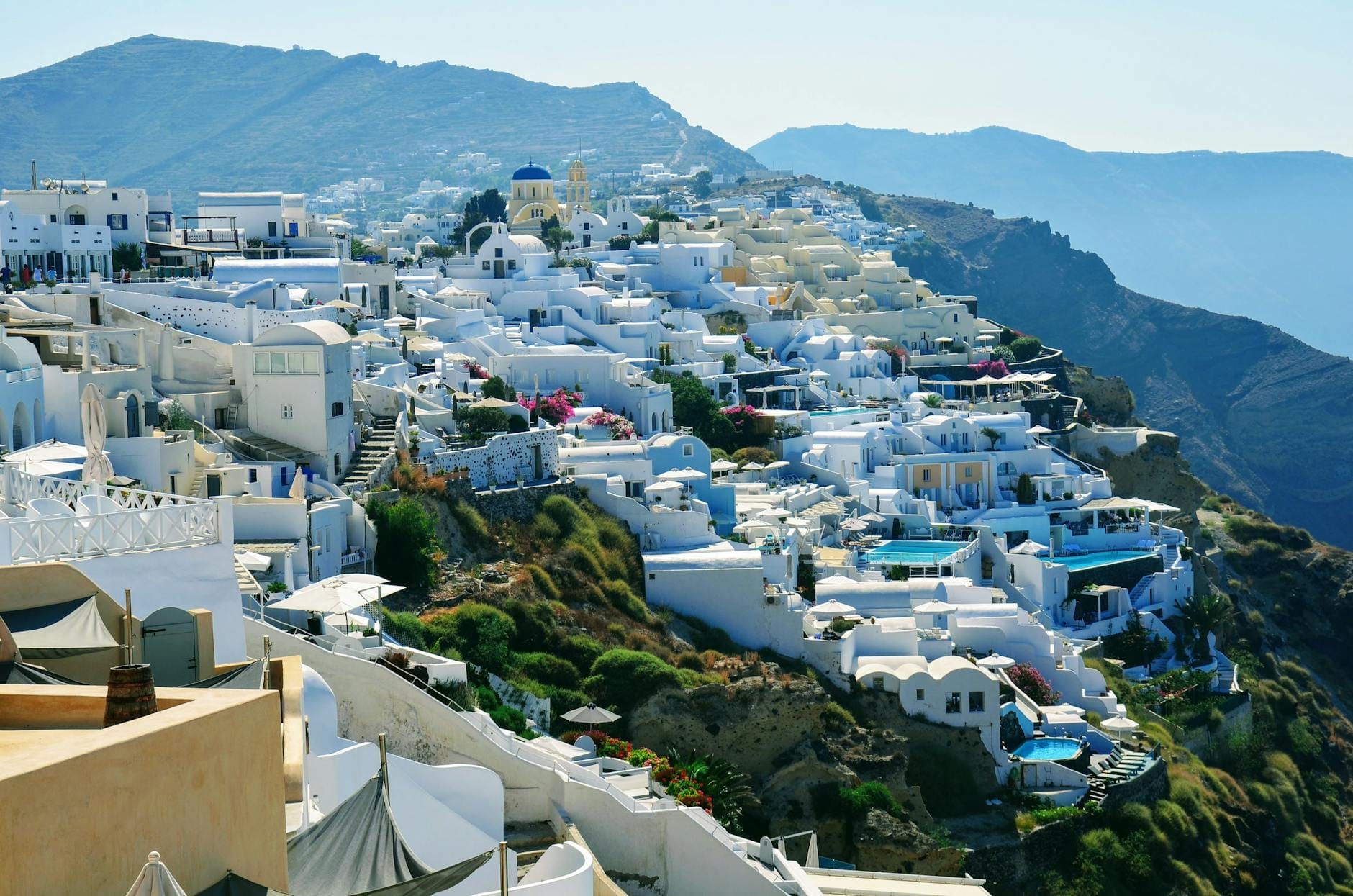 Vista panorâmica das famosas falésias da caldeira de Santorini, com hotéis e vilas caiadas em branco descendo pela encosta em direção ao mar azul e reluzente.