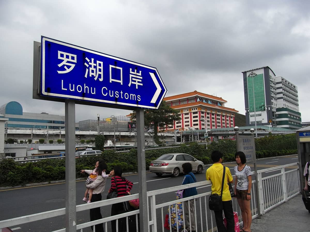 Vista ao nível da rua da travessia fronteiriça da Alfândega de Luohu com um proeminente letreiro azul, viajantes, veículos e edifícios em Shenzhen perto da fronteira com Hong Kong.
