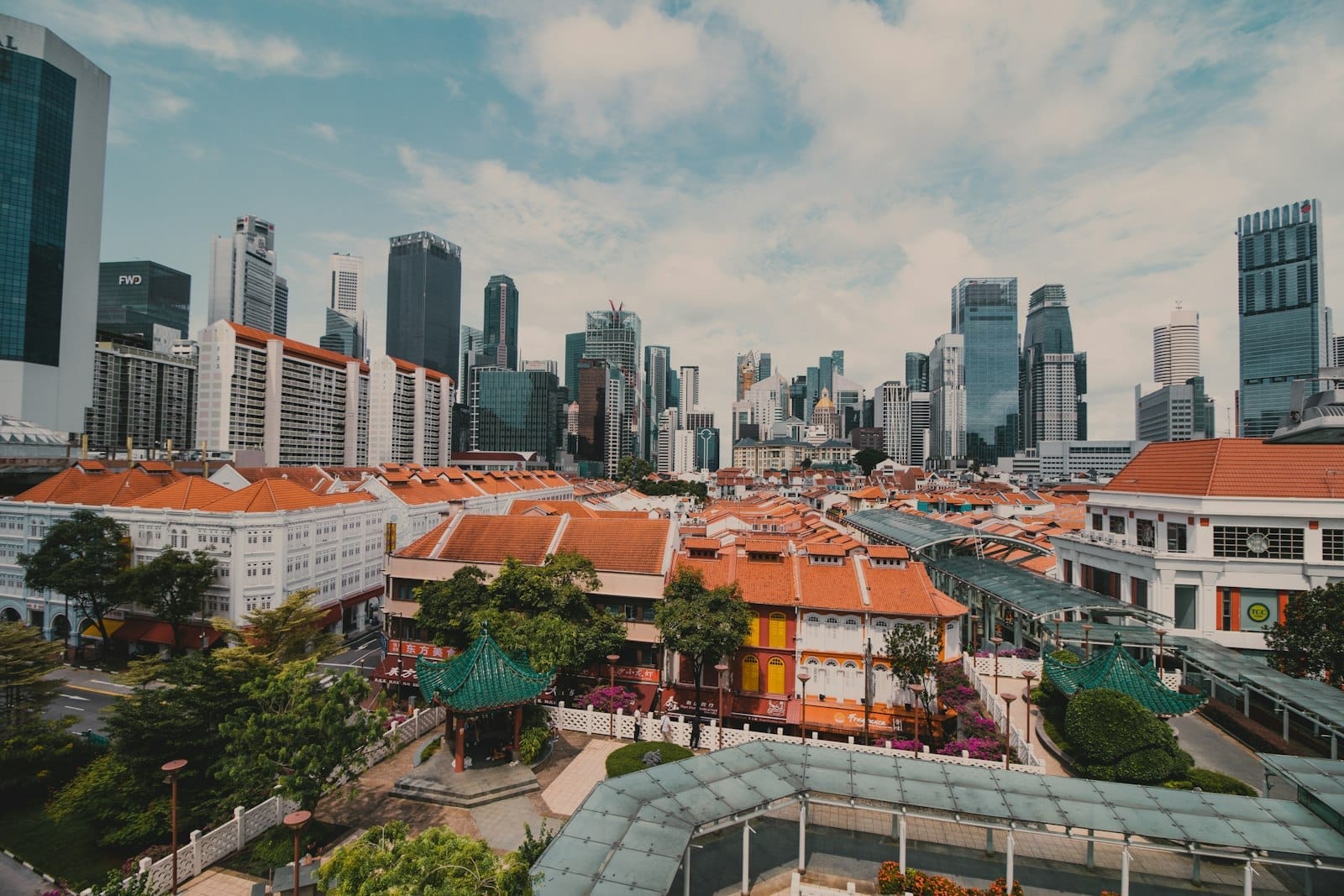 Vista panorâmica do skyline de Singapura, misturando arranha-céus modernos e shophouses históricas com telhados vermelhos, destacando bairros diversos sob um céu claro.