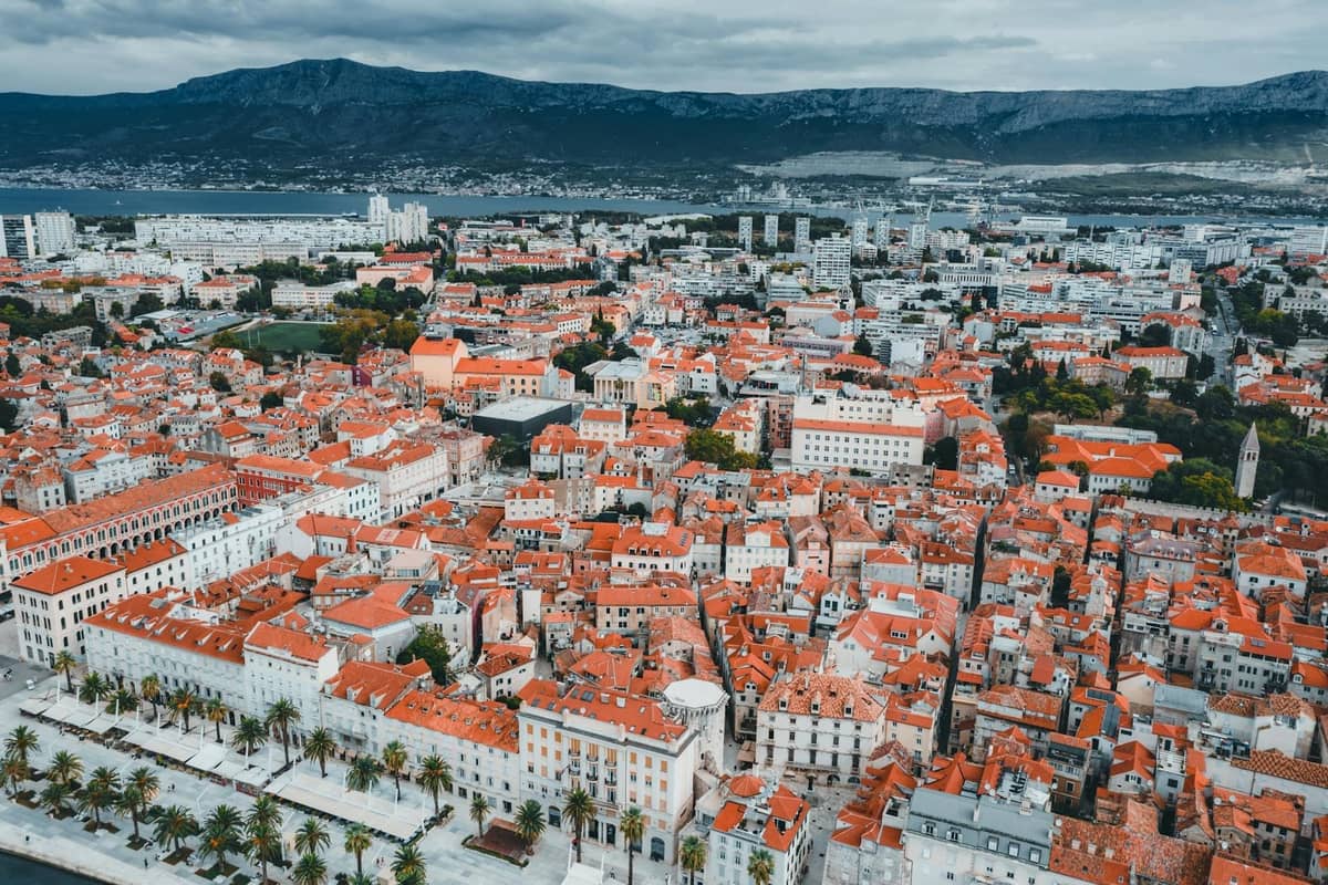 Luftaufnahme von Split, Kroatien, mit der kompakten Altstadt, rotbedachten Gebäuden, der zentralen Promenade und den umliegenden Vierteln mit Bergen in der Ferne.