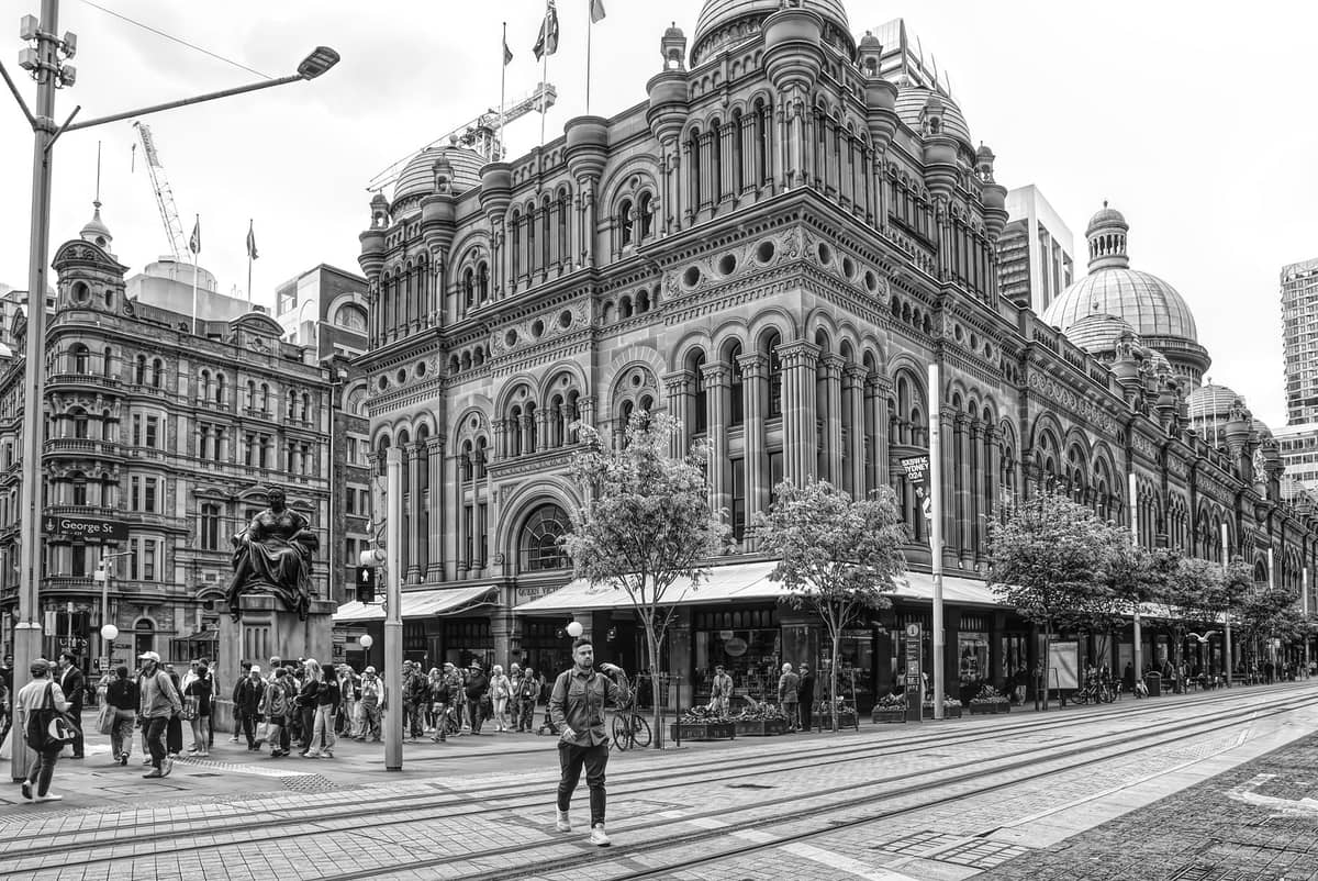 Black and white photo of the Queen Victoria Building in Sydney CBD with people walking and trams passing by in front.