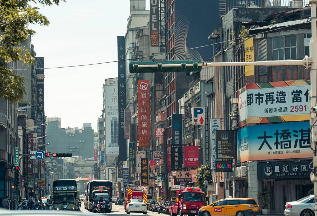 Belebte Straßenszene in Taipei mit Hotels, Läden, Taxis, Bussen, Rollern und chinesischen Schildern – ein typischer Block im Stadtzentrum am Tag.