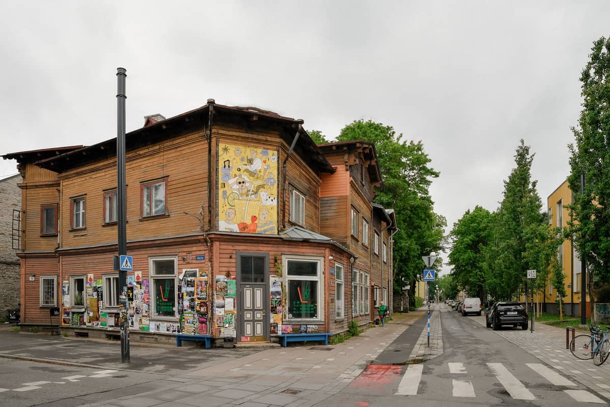 Straßenansicht eines bunten Holzgebäudes in Kalamaja mit Wandgemälde, Postern und nahegelegenem Übergang im Kreativviertel von Tallinn