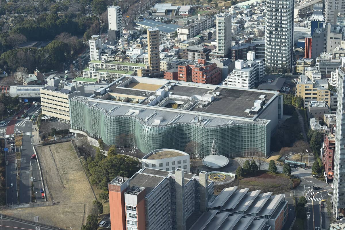 Aerial view of the National Art Center Tokyo, a distinctive modern glass building surrounded by city streets and apartment buildings in Roppongi.