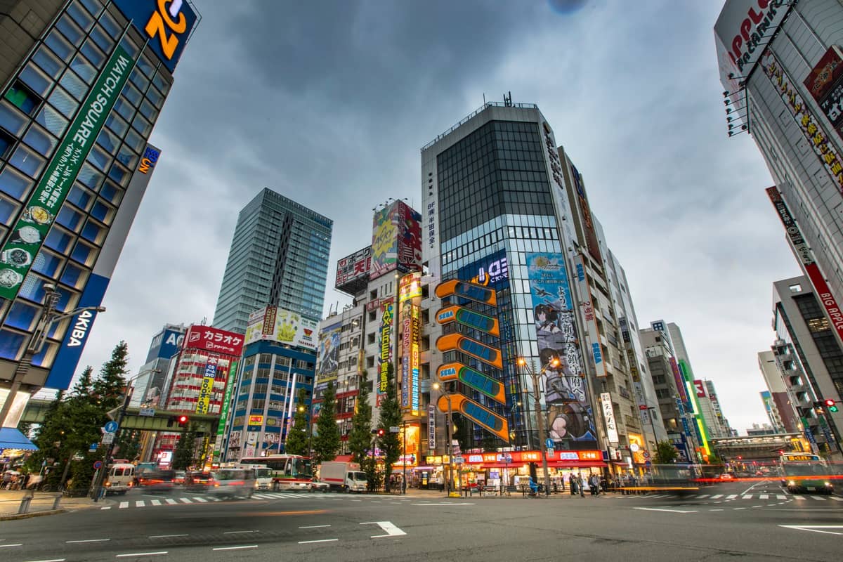 Wide urban view of Shinjuku district in Tokyo with busy streets, colorful signs, and modern high-rise buildings under a cloudy sky.