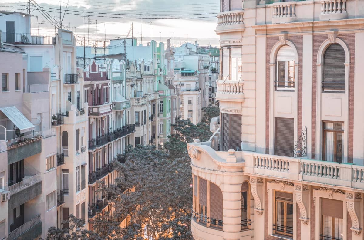 Des immeubles d'appartements aux couleurs pastel avec des balcons bordent une rue verdoyante dans un quartier classique de Valencia, illustrant l'architecture résidentielle locale typique.