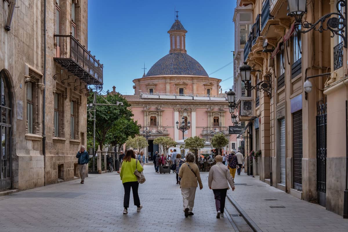 Des personnes se promenant dans une rue piétonne du vieux quartier historique de Valencia avec un bâtiment d'église à dôme en arrière-plan.