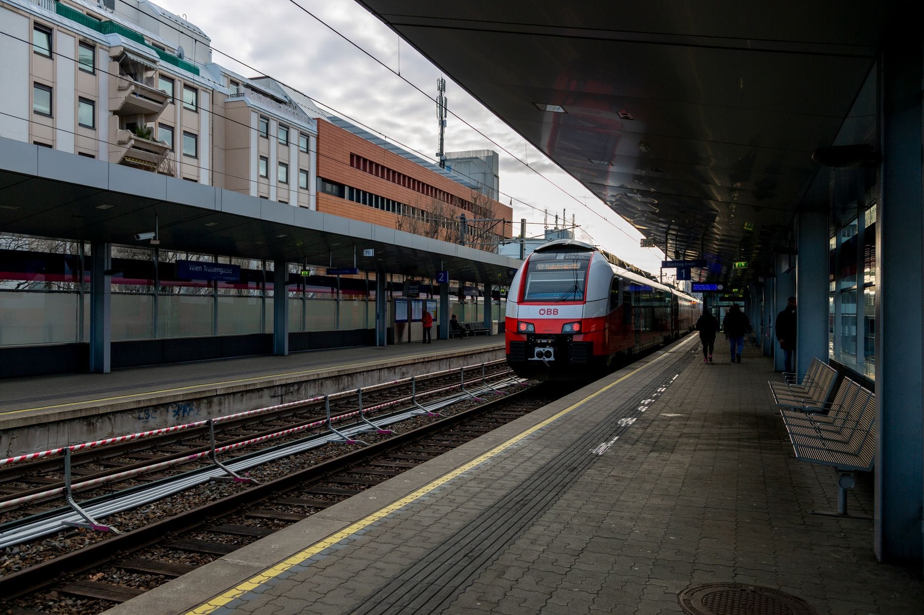 Ein moderner österreichischer ÖBB-Zug auf einem Wiener S-Bahn-Bahnsteig, der sich mit städtischen Gebäuden im Hintergrund zur Abfahrt bereit macht.