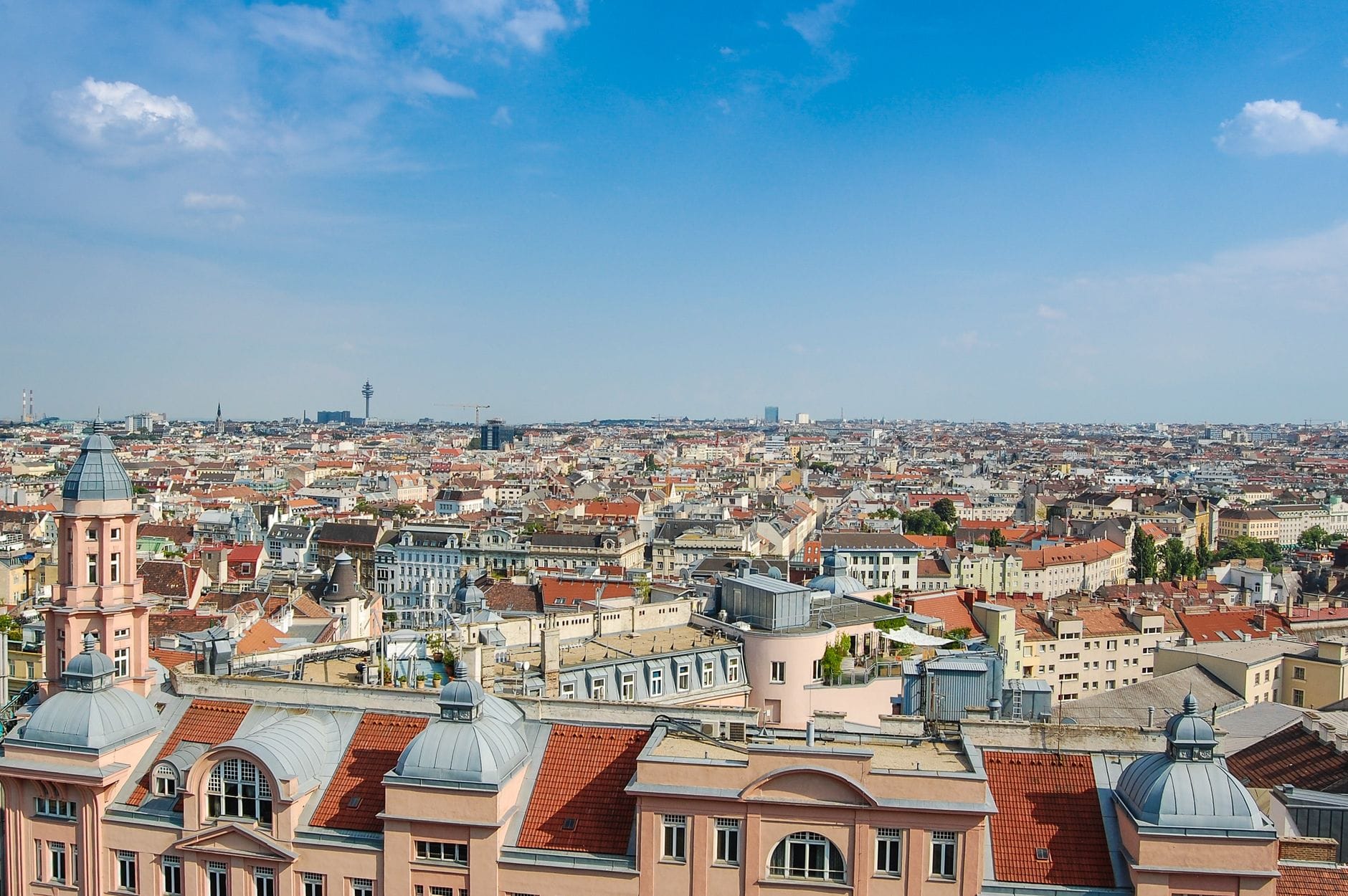 Ein weiter Blick aus der Vogelperspektive über die Wiener Dächer unter strahlend blauem Himmel, der die vielfältigen Stadtteile und die ikonische Architektur der Stadt einfängt.