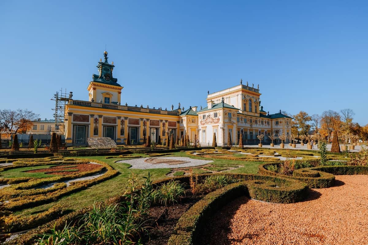Palacio de Wilanów en Varsovia con elegantes jardines barrocos y cielo azul despejado, mostrando el ambiente tranquilo e histórico del distrito.