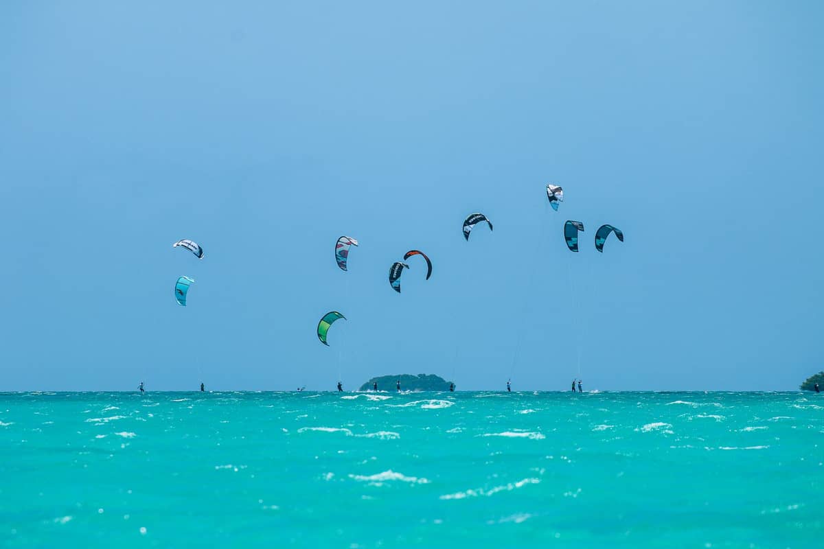 Türkisfarbenes Meer mit mehreren Kitesurfern und bunten Drachen unter einem klaren blauen Himmel, das die Kitesurfszene an der Südostküste Sansibars heraufbeschwört.