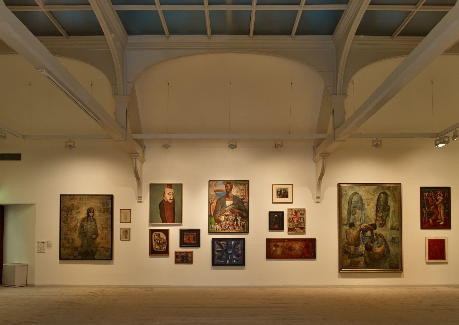 Vista ampia di una parete espositiva alla Whitechapel Gallery, con varie opere d'arte contemporanea sotto soffitti ad arco alti e illuminazione soffusa.