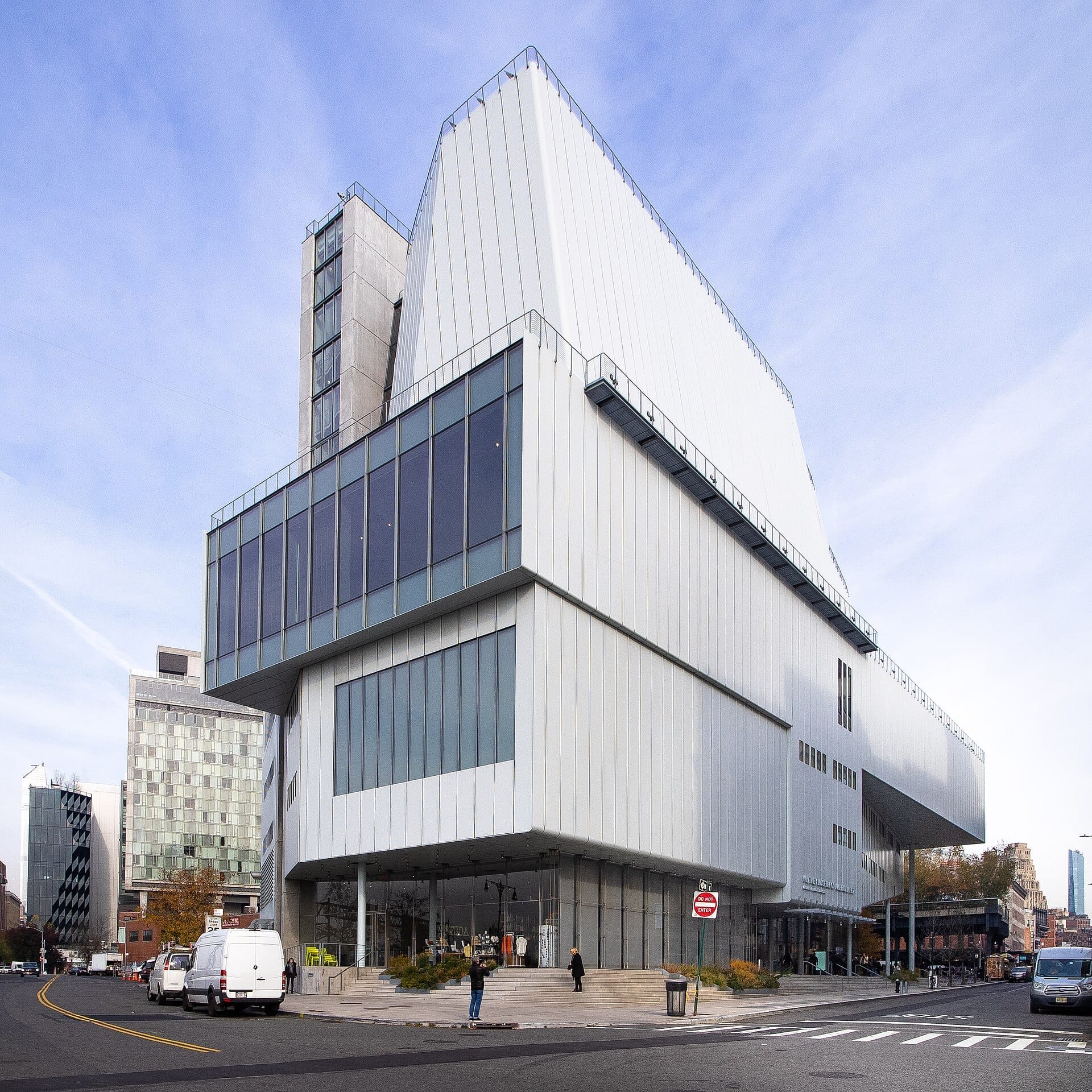 L'imponente esterno moderno del Whitney Museum of American Art, con pannelli di vetro e metallo, si erge su una strada cittadina sotto un cielo azzurro terso.