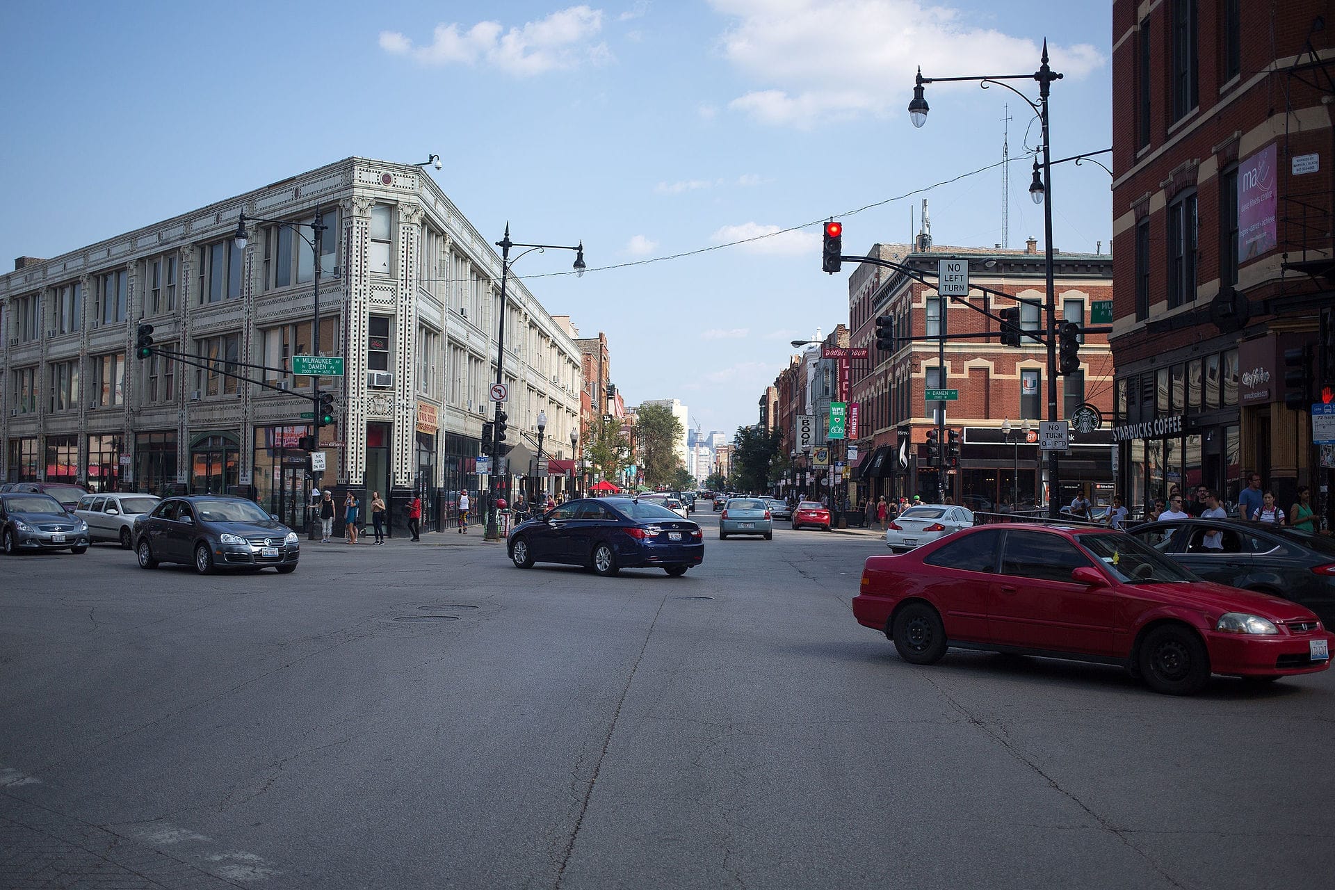 ทางแยกที่คึกคักใน Wicker Park, Chicago พร้อมอาคารหินสีเทาที่มีประวัติศาสตร์ ป้ายถนน รถยนต์ คนเดินถนน และ Starbucks ในวันที่แดดสดใส