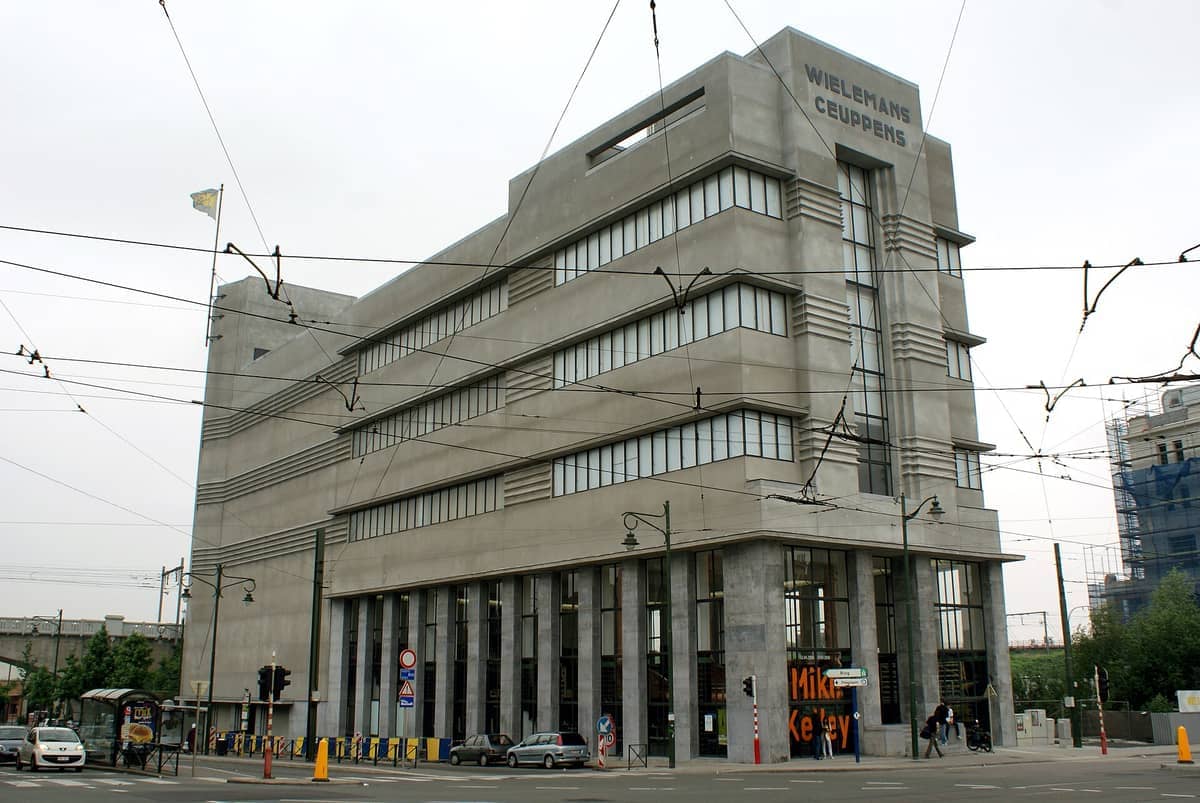 Vista exterior do WIELS Centre d'Art Contemporain em Bruxelas, um grande edifício Art Déco cinzento com linhas angulares e janelas altas num dia nublado.