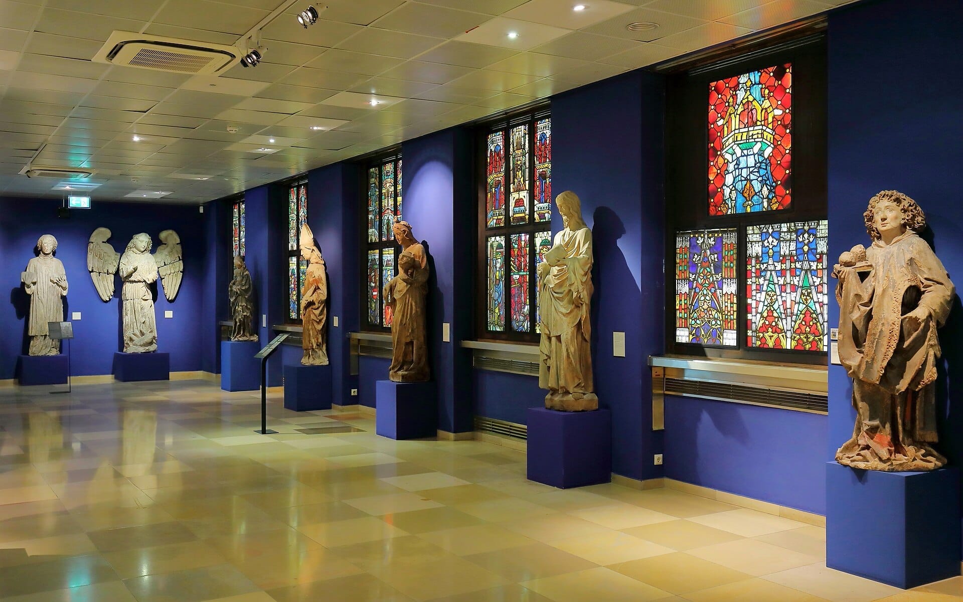 Steinstatuen und lebhafte Buntglasfenster entlang einer blauen Wand im neu renovierten Wien Museum in Wien.