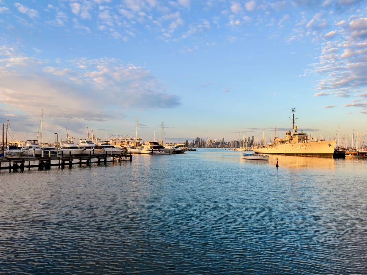 Williamstown Foreshore in der goldenen Stunde mit historischem Kriegsschiff, Marina, Melbourner Skyline und Piers des maritimen Viertels.