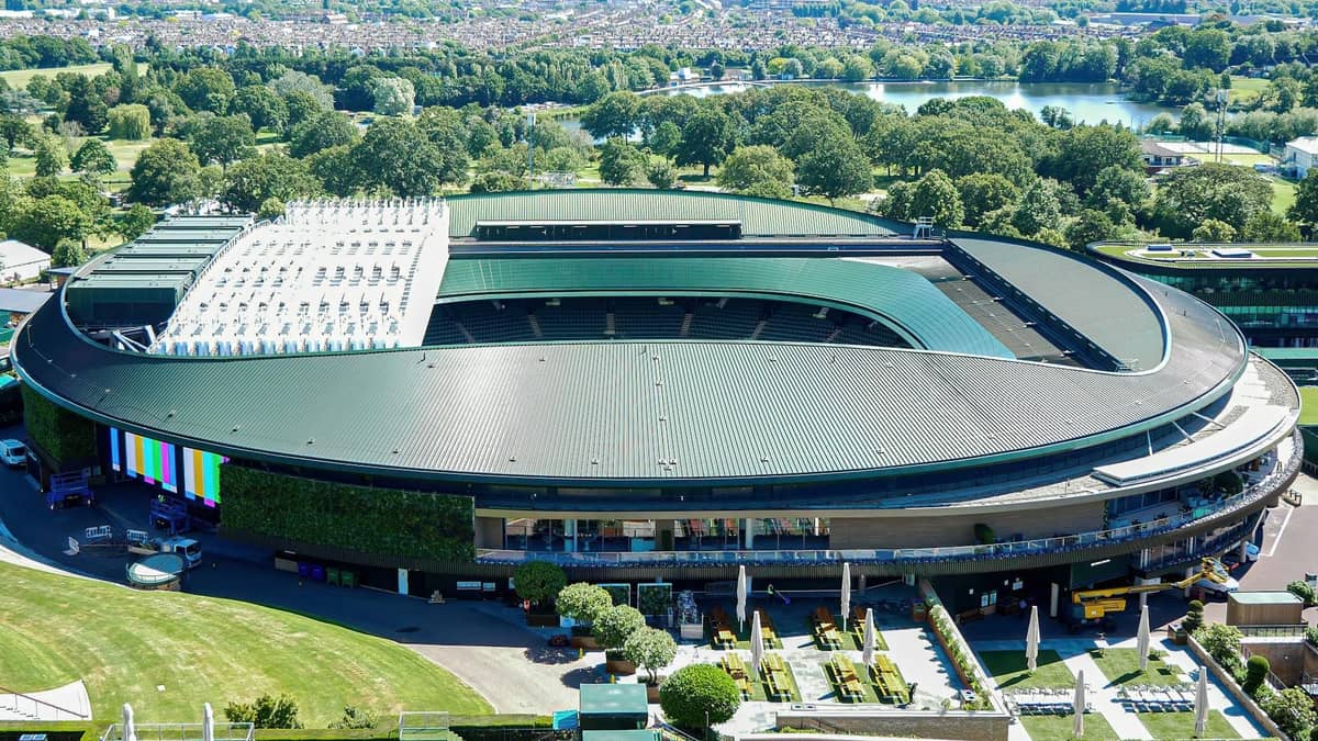 Vista aérea da quadra central de Wimbledon no All England Lawn Tennis Club com campos verdes e árvores ao redor.