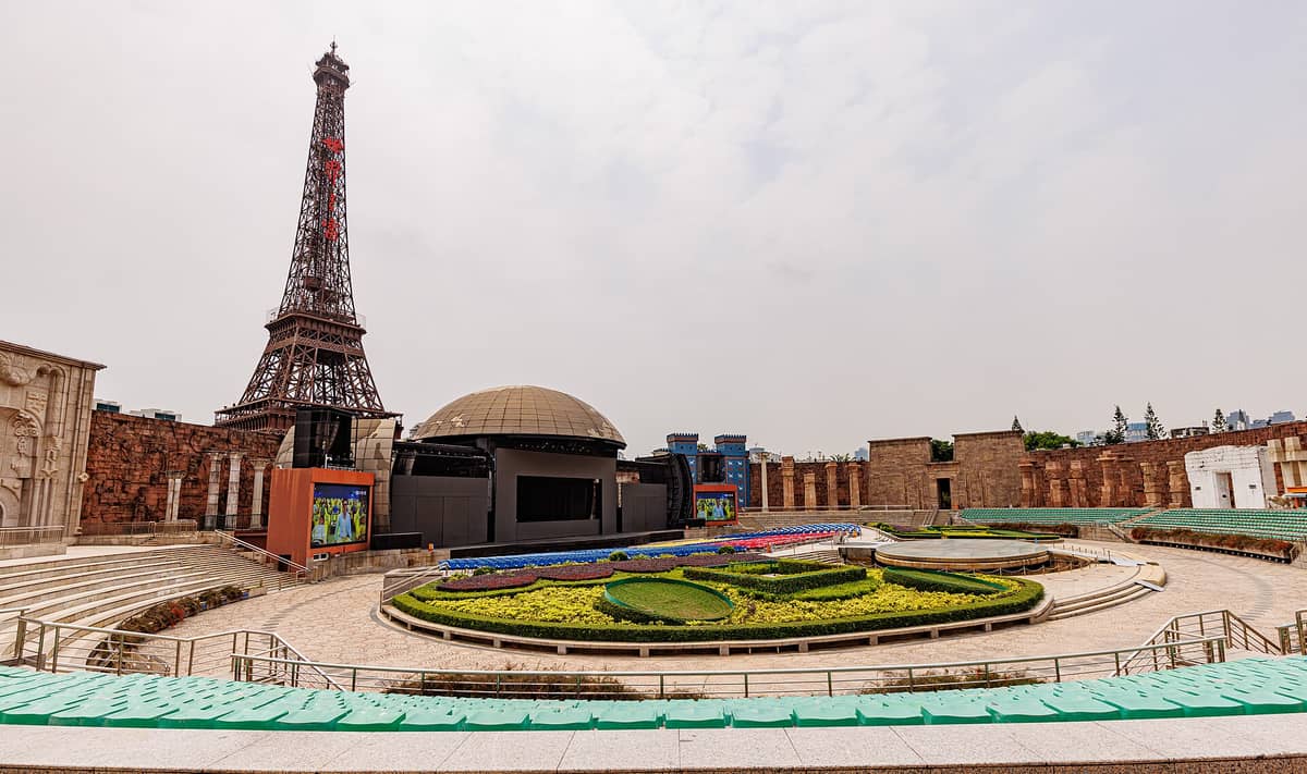 Vista ampla do teatro a céu aberto da Janela do Mundo em Shenzhen com a réplica da Torre Eiffel ao fundo e jardins geométricos em primeiro plano.