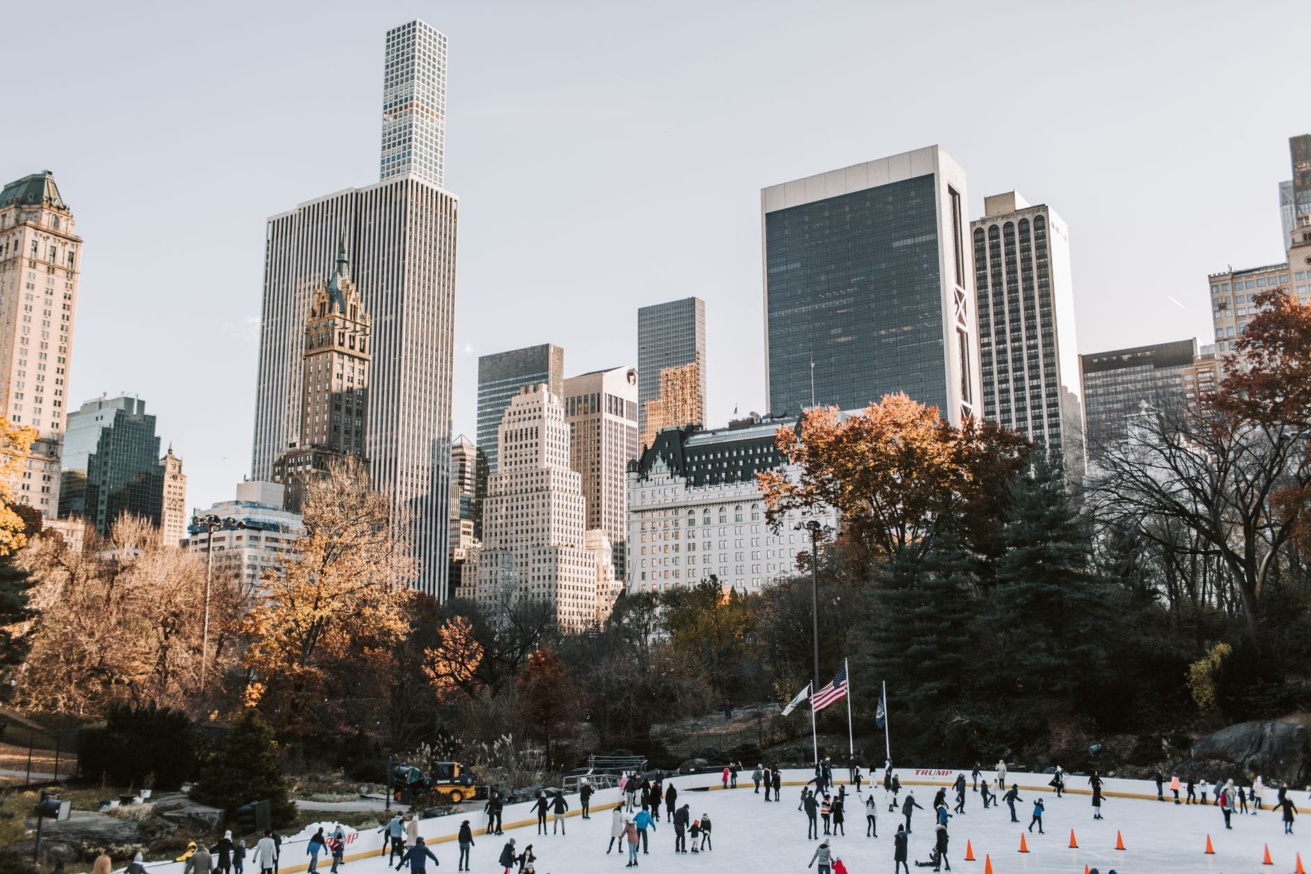 Folla di persone che pattina alla Wollman Rink di Central Park con i grattacieli di Manhattan sullo sfondo in una limpida giornata autunnale o invernale.
