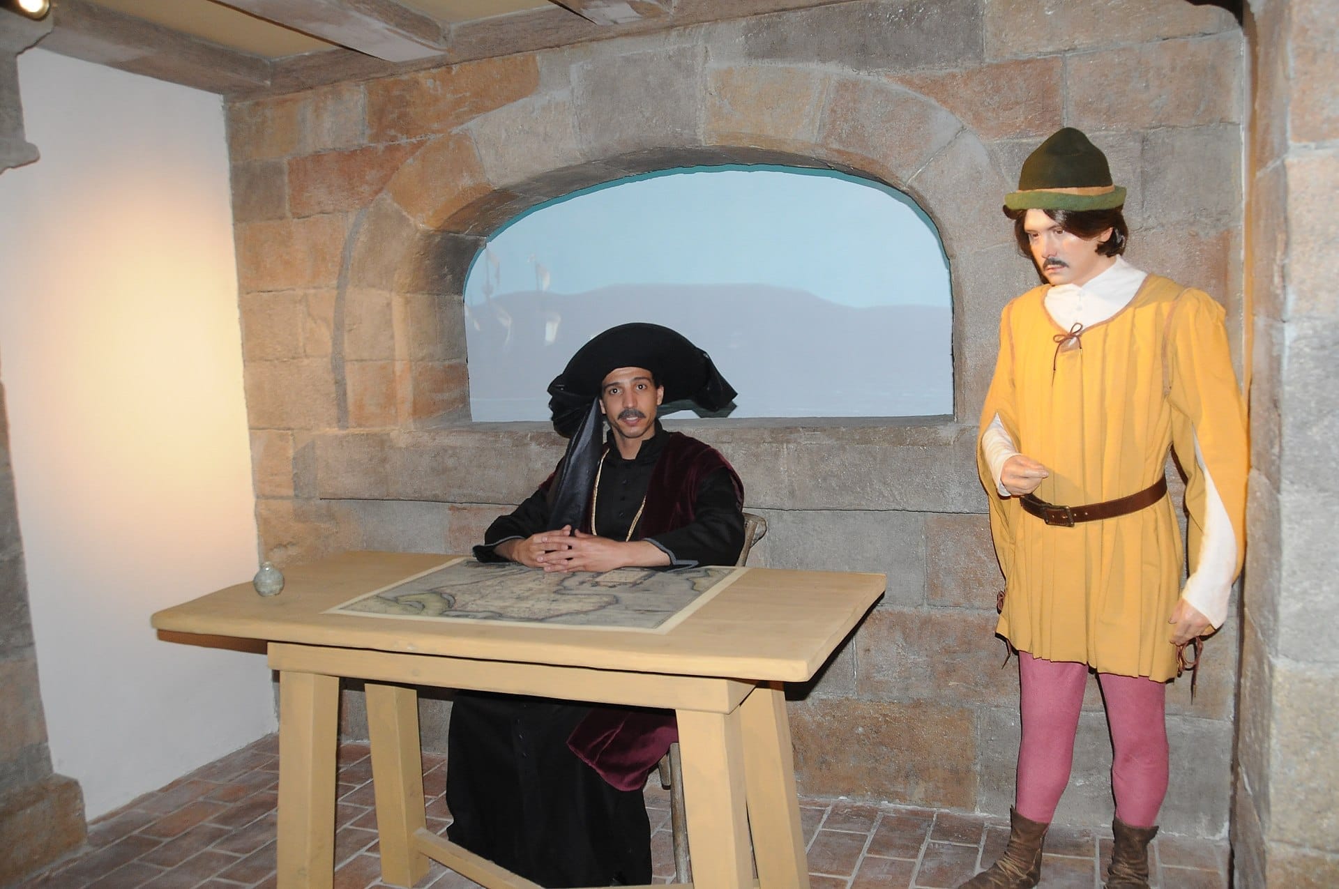 Manichini realistici vestiti da esploratori portoghesi in abiti d'epoca all'interno di una sala espositiva con pareti in pietra al museo World of Discoveries di Porto.