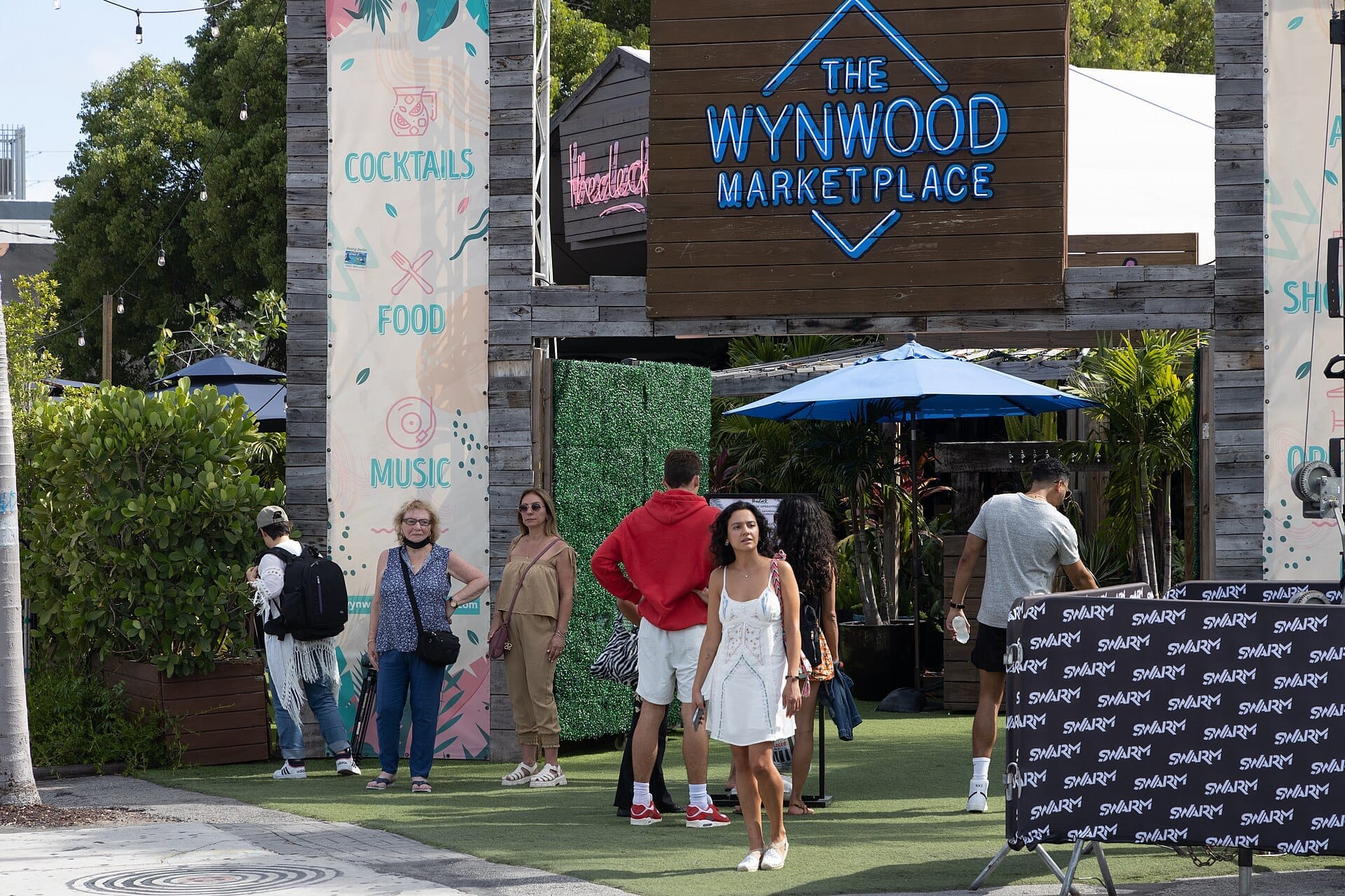 Ingresso al Wynwood Marketplace a Miami con gruppi di persone vestite in modo casual, segnaletica vivace e vegetazione tropicale alla luce del giorno.